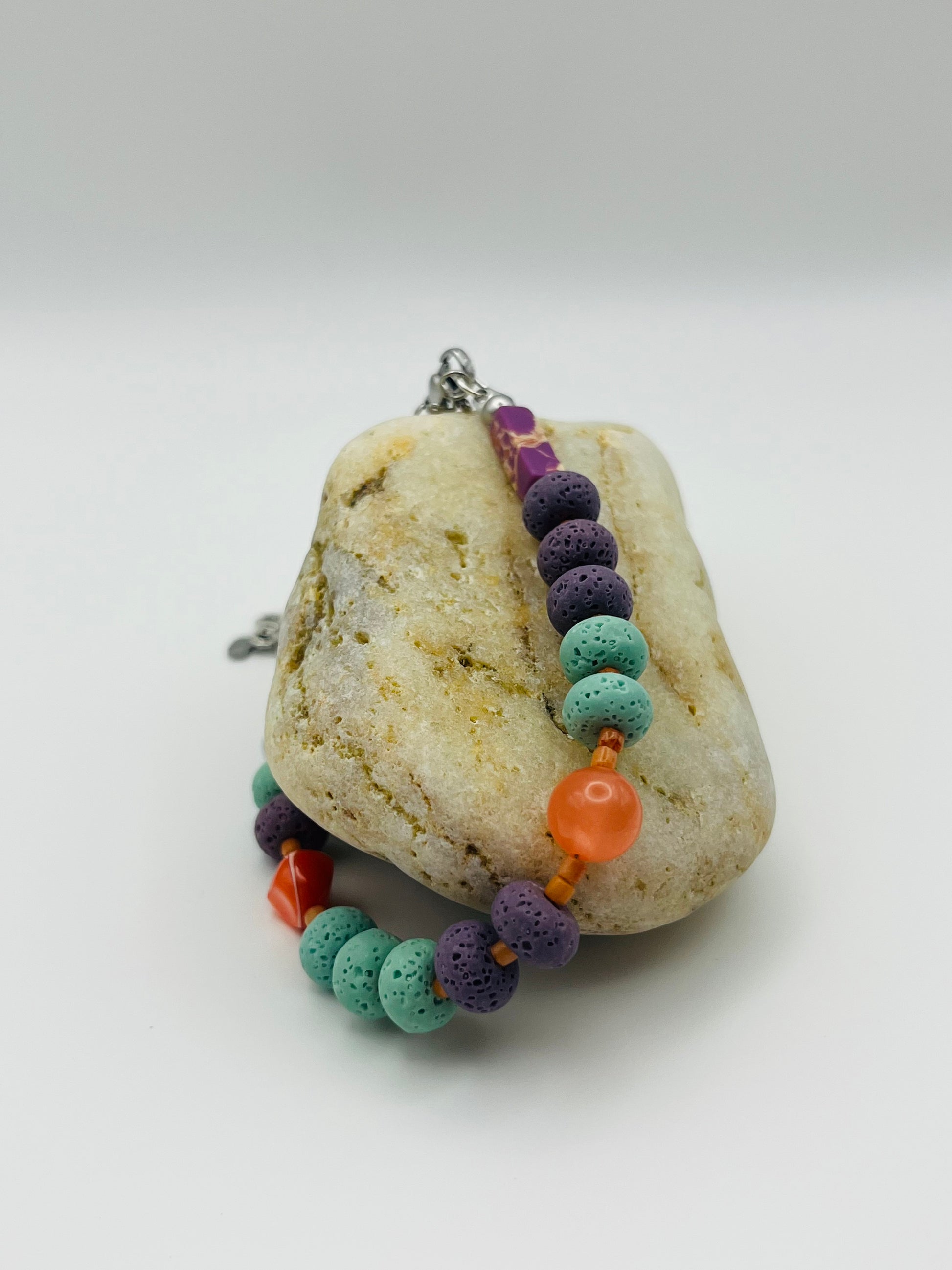 Pulsera artesanal Arrecife sobre piedra, con lava volcánica turquesa y morada, cornalina naranja y coral rojo, montada a mano en Murcia
