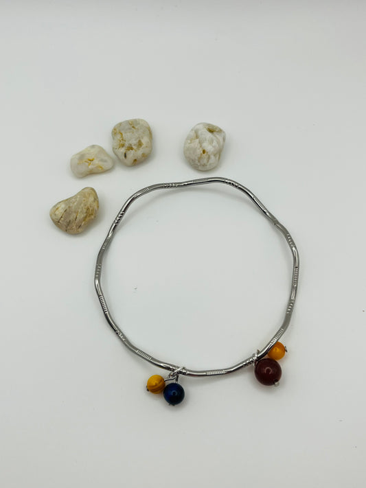 Pulsera artesanal Cala en aro rígido plateado con colgantes de lapislázuli azul, ágata roja y ágata amarilla sobre fondo blanco, montada a mano en Murcia
