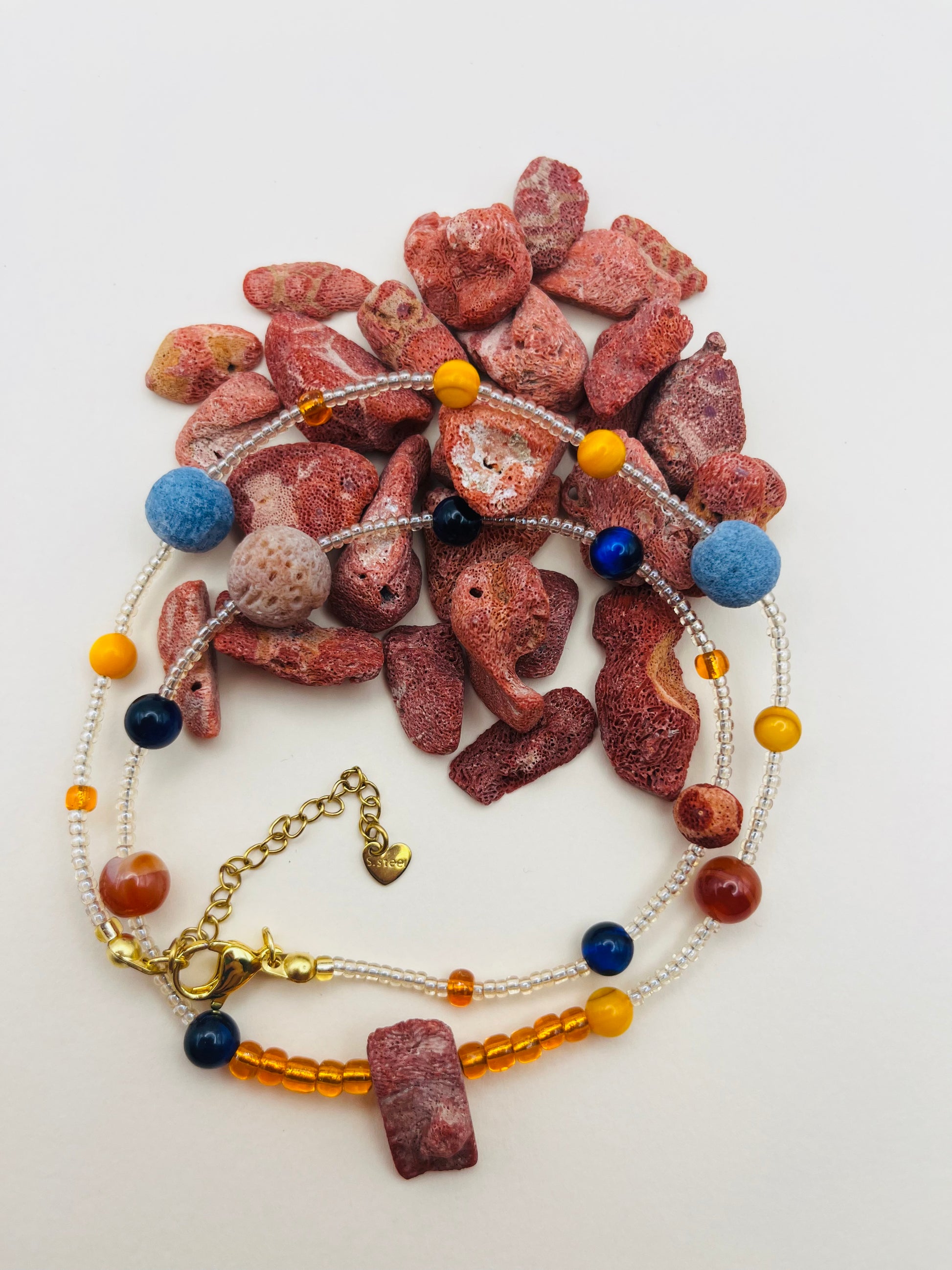 Pulsera Cala – semillas de rocalla transparentes con lava volcánica azul y terracota, ámbar amarillo, lapislázuli azul marino y coral rojo natural, cierre dorado, hecha a mano en Murcia