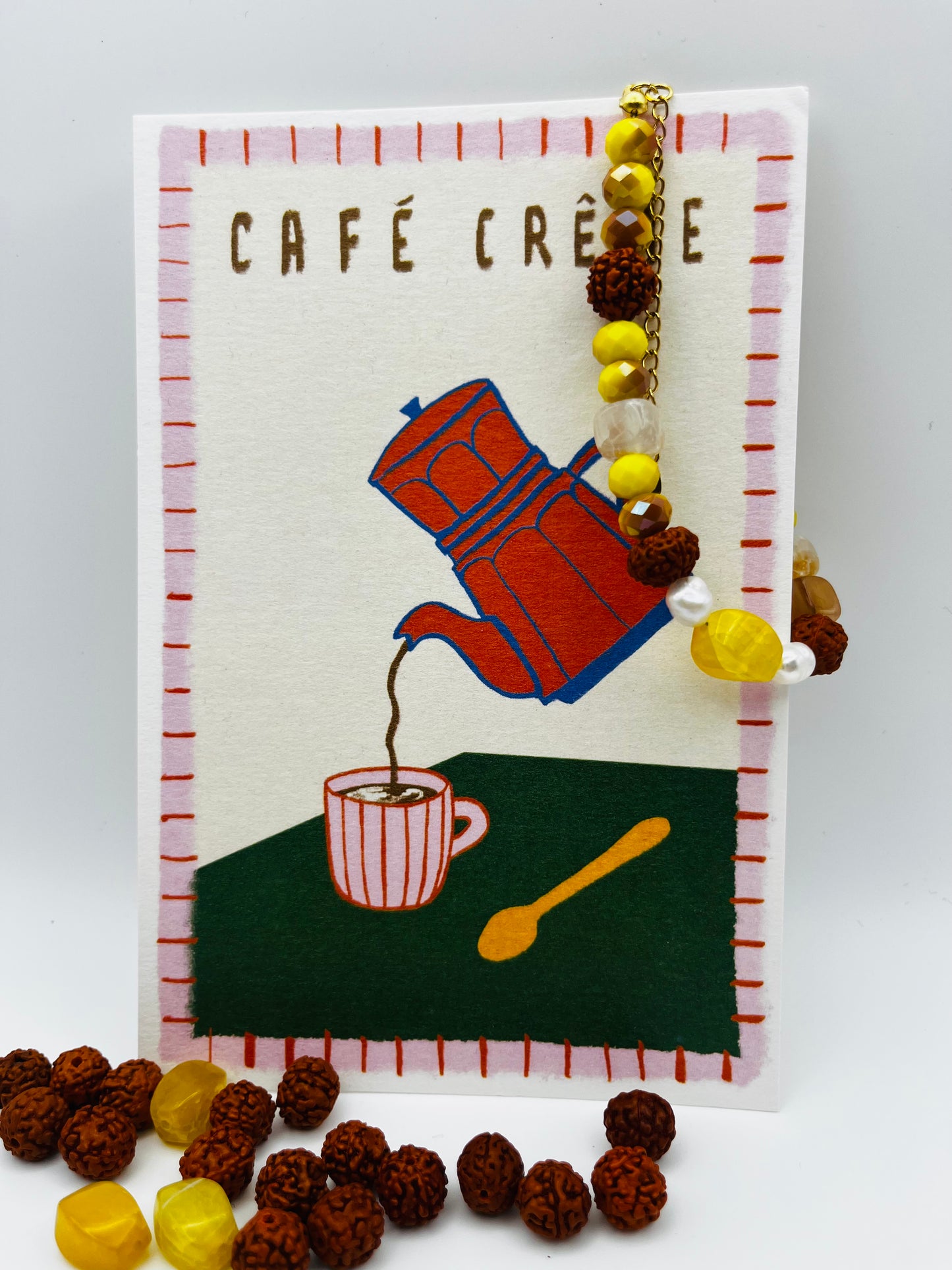 Pulsera artesanal Calima con semillas de rudraksha, cristal amarillo y nácar, apoyada en ilustración de café, montada a mano en Murcia
