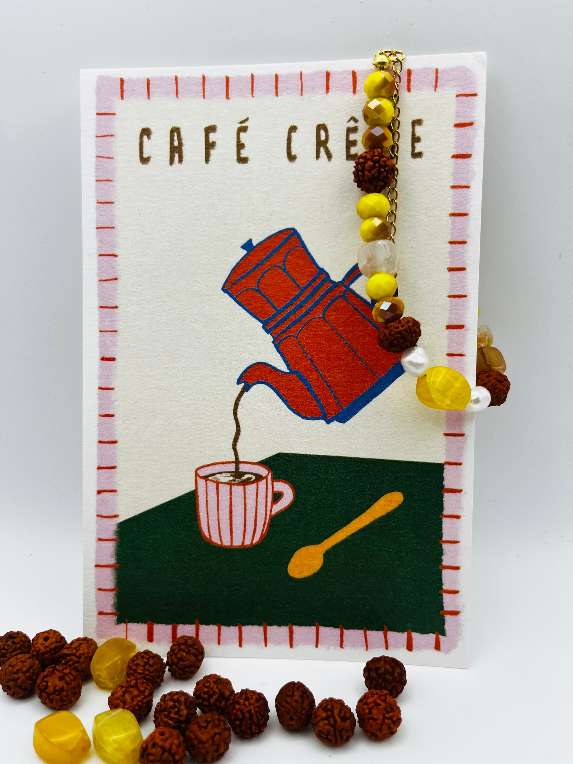 Pulsera artesanal Calima con semillas de rudraksha, cristal amarillo y nácar, apoyada en ilustración de café, montada a mano en Murcia
