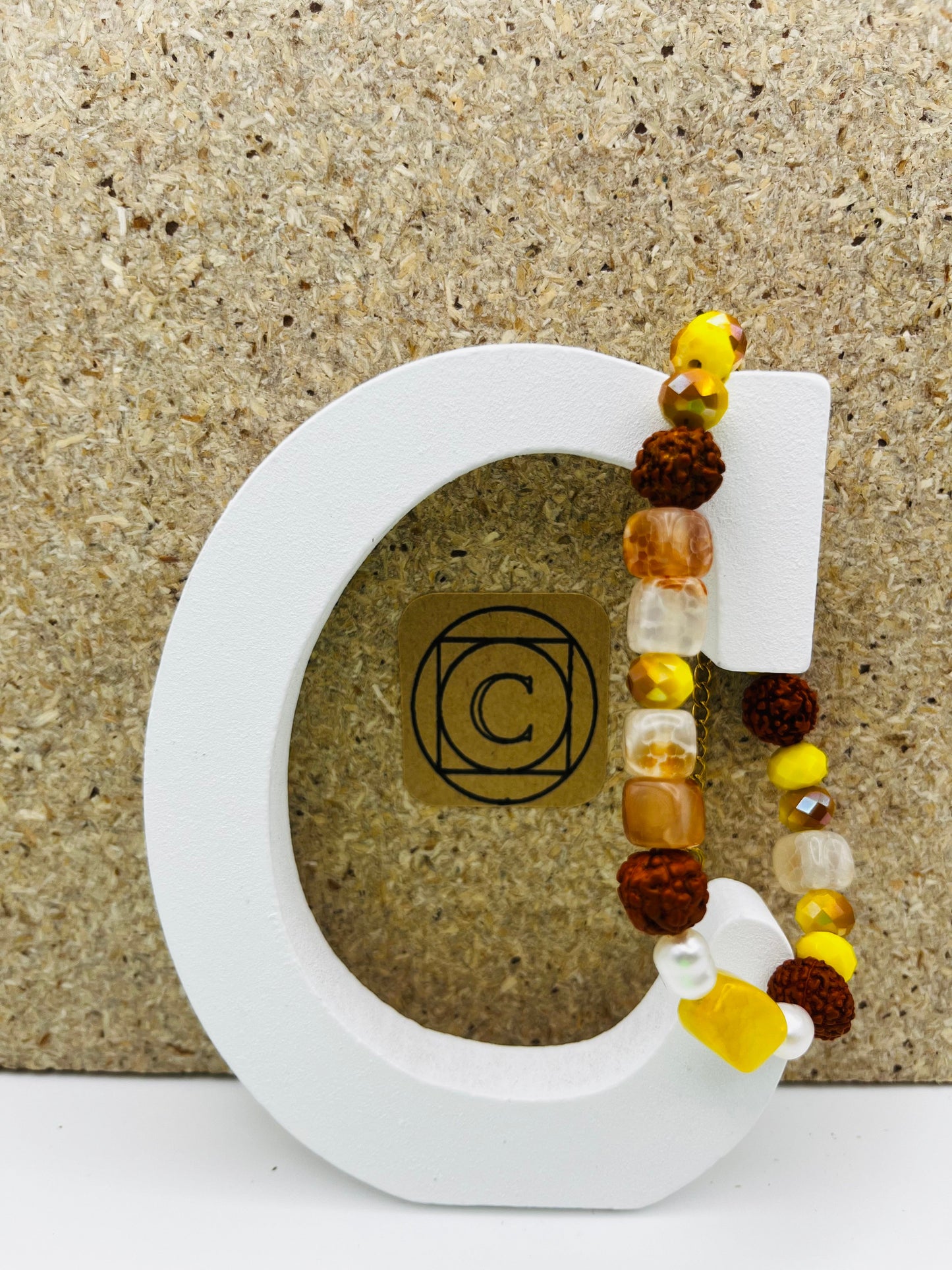 Pulsera artesanal Calima en aro rígido de acero con semillas de rudraksha, cristal facetado amarillo, nácar, cornalina y flor de cerámica blanca, montada a mano en Murcia
