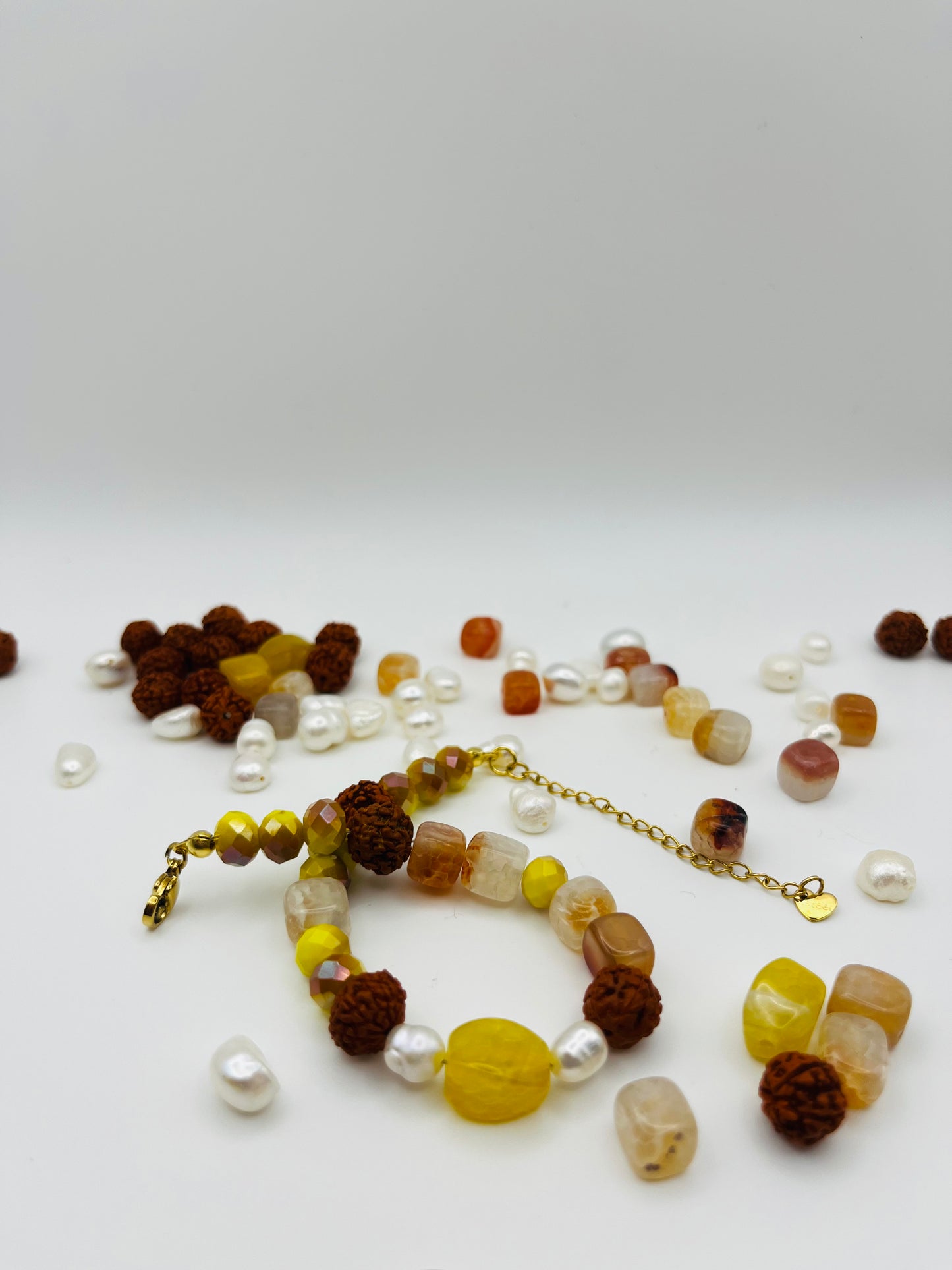 Pulsera artesanal Calima con semillas de rudraksha, cristal amarillo, nácar y cornalina, rodeada de los materiales naturales sueltos, montada a mano en Murcia
