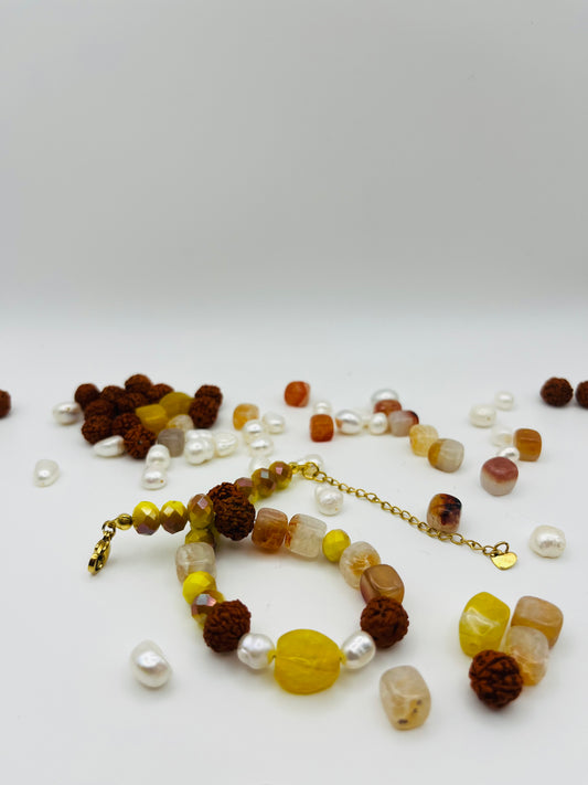 Pulsera artesanal Calima con semillas de rudraksha, cristal amarillo, nácar y cornalina, rodeada de los materiales naturales sueltos, montada a mano en Murcia
