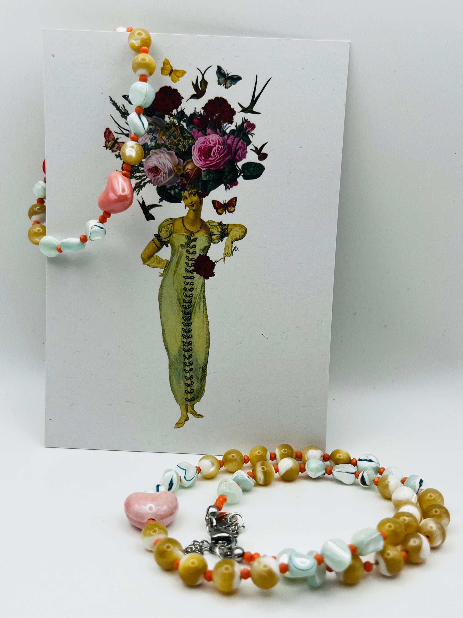 Conjunto artesanal Calma: pulsera y collar con howlita verde menta, coral naranja, howlita mostaza y corazón de cerámica rosa, junto a ilustración vintage Cuadratura, montados a mano en Murcia
