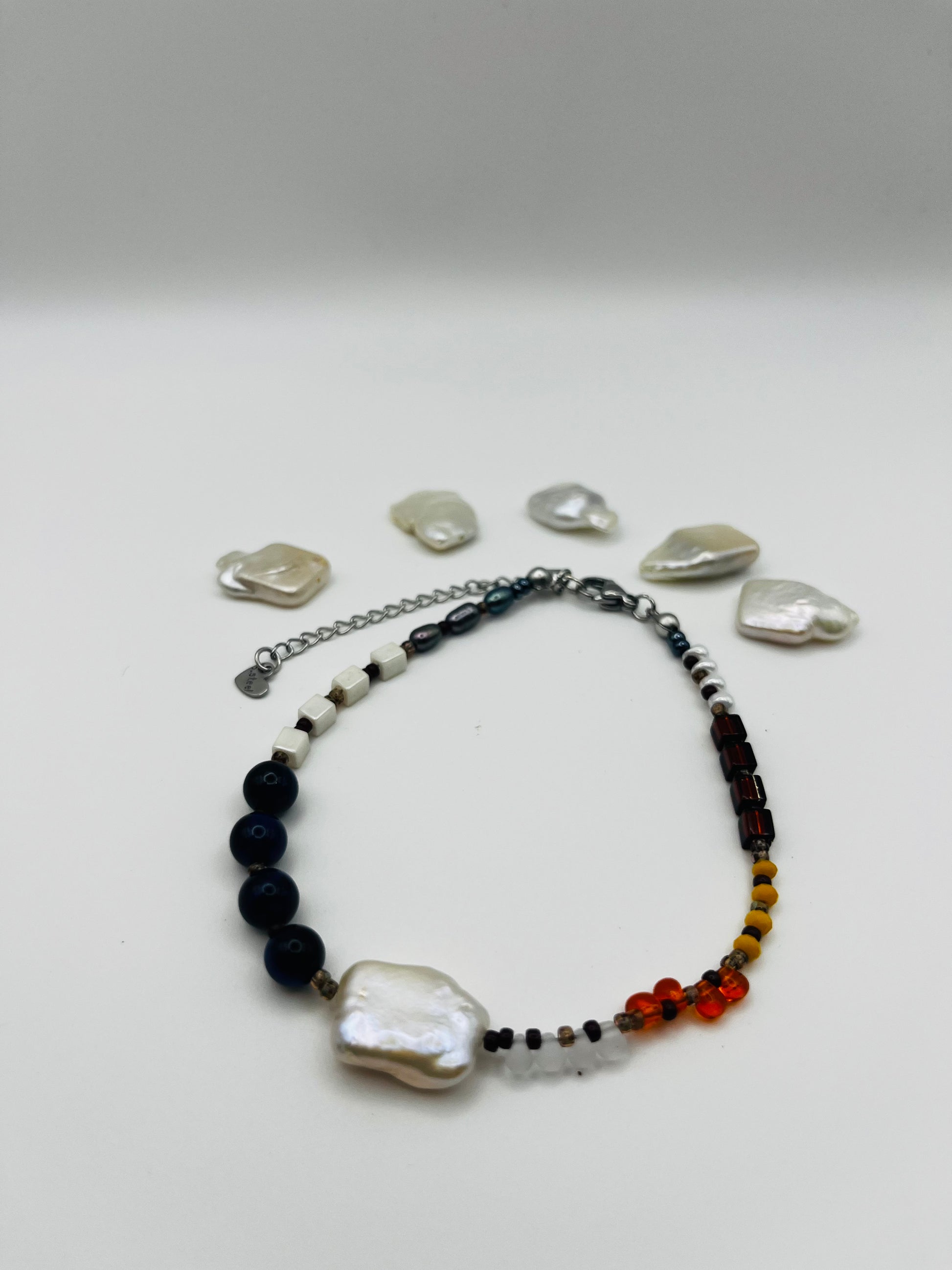 Pulsera artesanal Solana con perla barroca blanca, ónix azul marino, ámbar natural, cristal granate y amarillo, rodeada de perlas barrocas sueltas, montada a mano en Murcia
