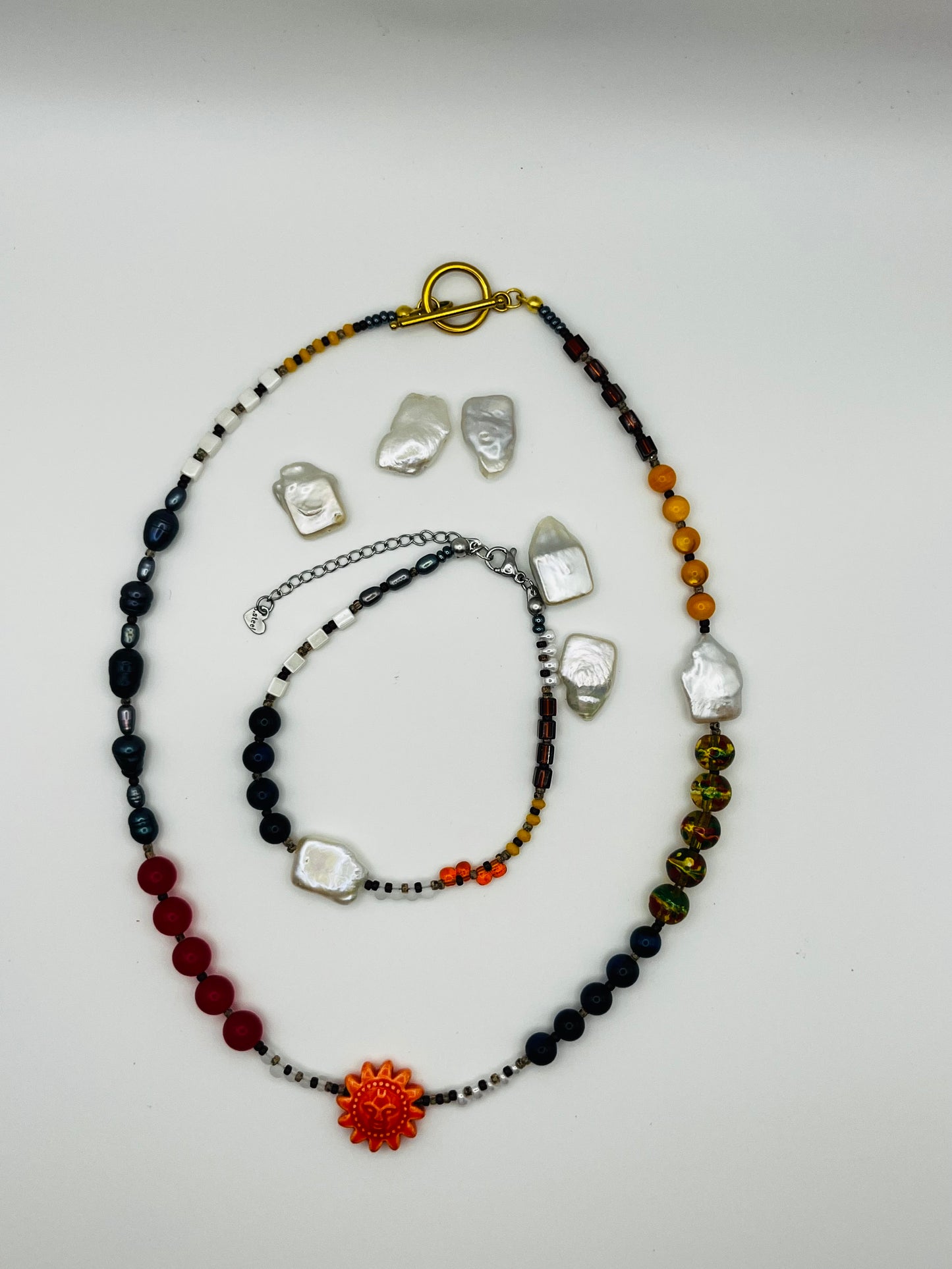Conjunto artesanal Solana: pulsera y collar con perla barroca, ónix, ámbar, cristal y colgante sol de cerámica naranja con cierre toggle dorado, montados a mano en Murcia

