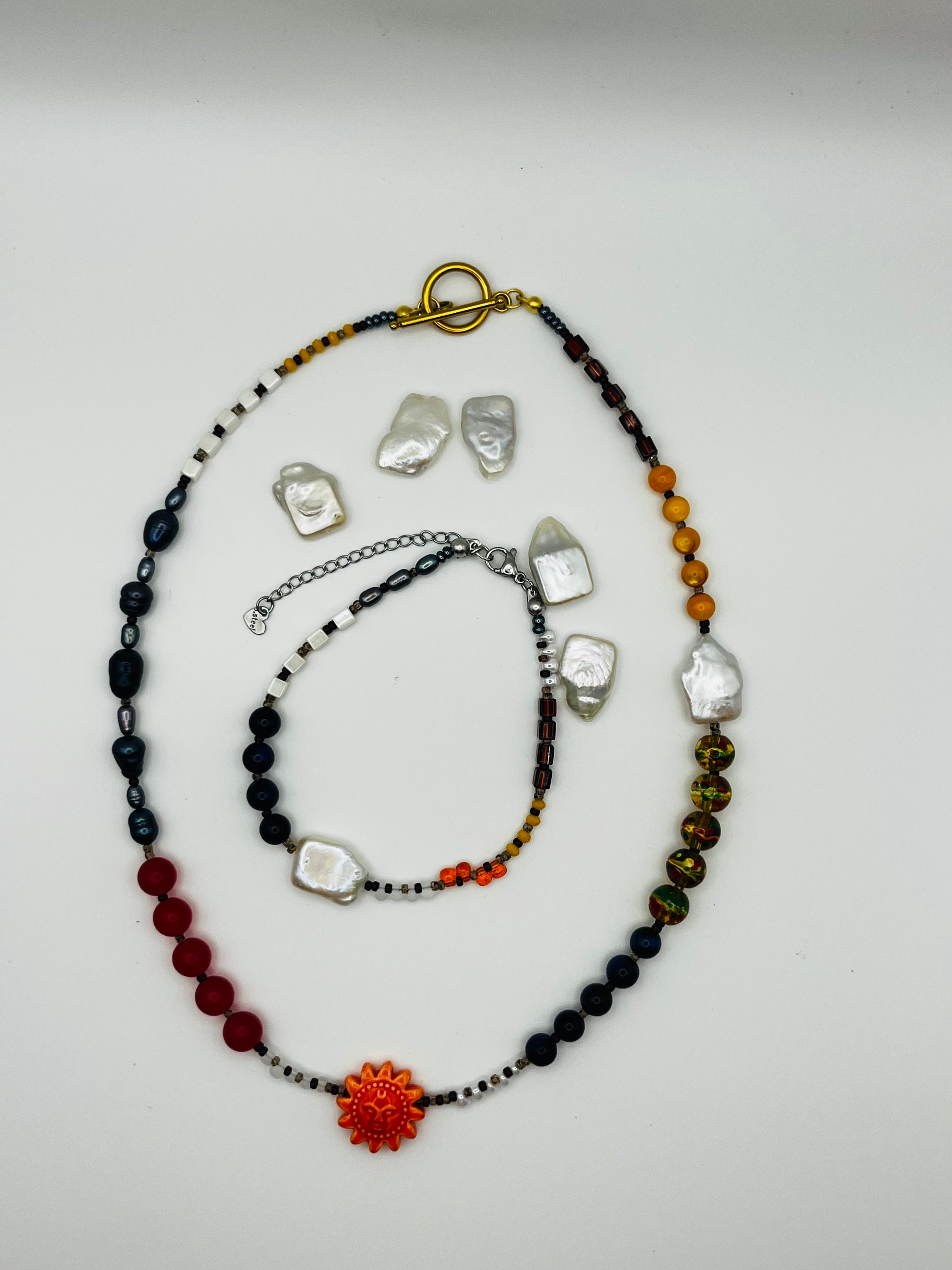 Conjunto artesanal Solana: pulsera y collar con perla barroca, ónix, ámbar, cristal y colgante sol de cerámica naranja con cierre toggle dorado, montados a mano en Murcia
